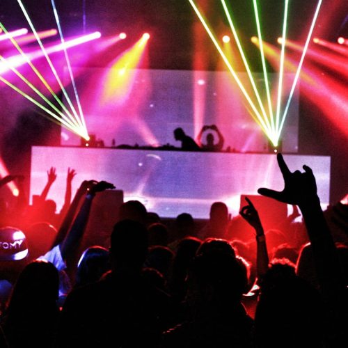 Energetic nightclub scene with laser lights and a lively crowd dancing to EDM music.